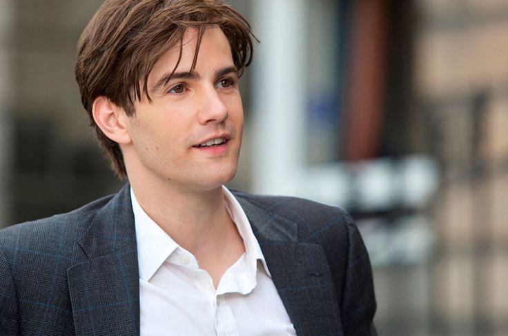 a man wearing a suit and white shirt is talking to someone on the street with his hand in his pocket