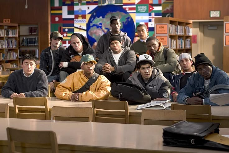 a group of young men sitting at desks in a library with bookshelves