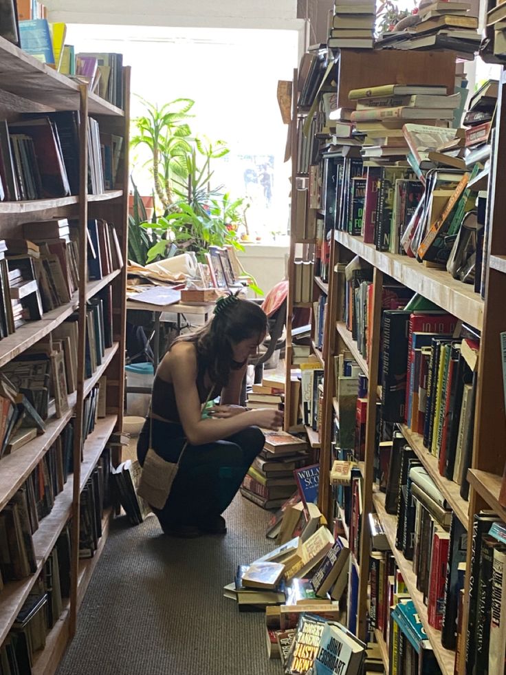 a woman sitting on the floor in front of a bookshelf full of books