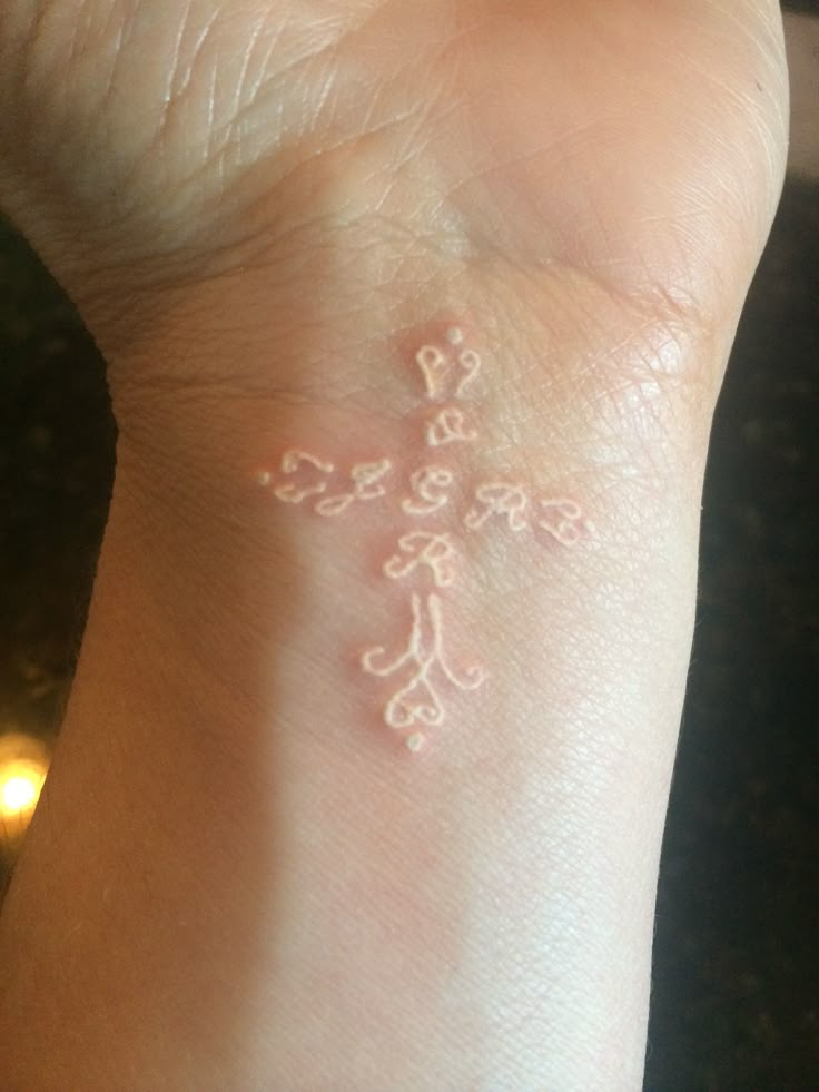 a person's wrist with a small tattoo on it that has an image of a cross in the middle