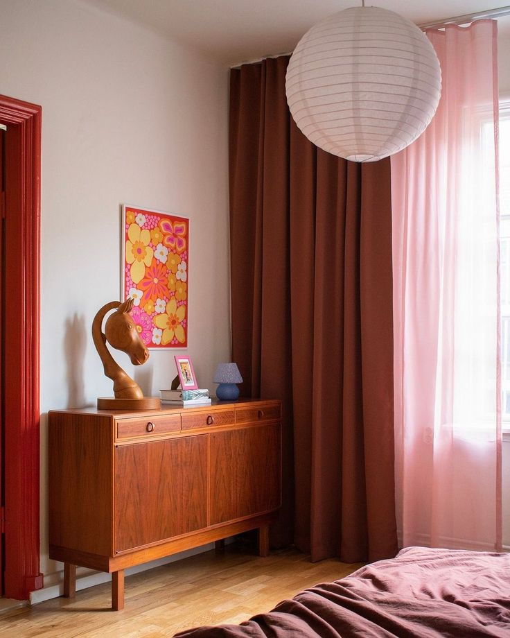 a bedroom with red curtains and a wooden dresser in front of a window that has a painting on it