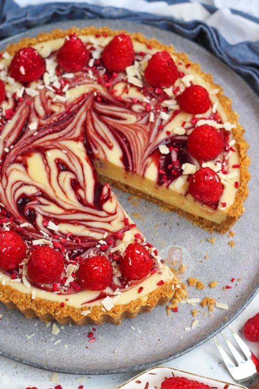 a cheesecake topped with raspberries on top of a metal tray next to a fork