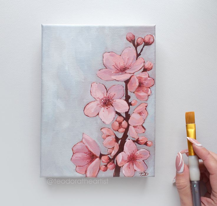 a person holding a paintbrush next to a painting with pink flowers on it