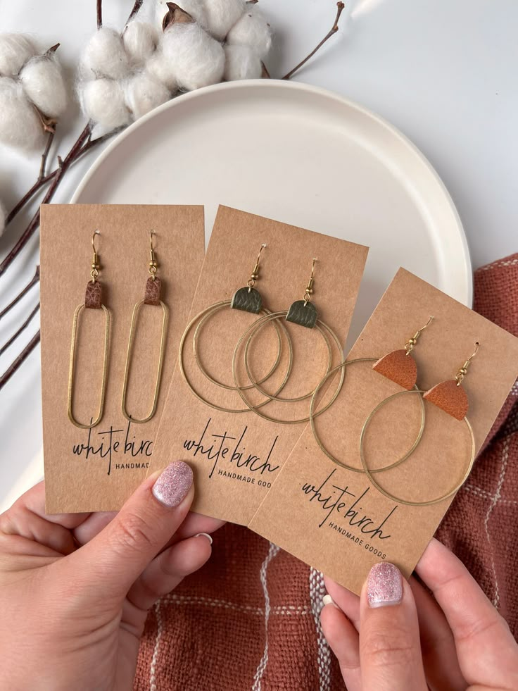 three pairs of earrings are being held up by two hands on a plate with cotton