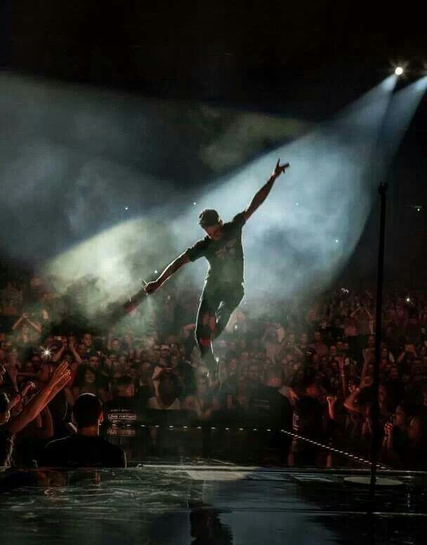 a man is performing on stage with his arms in the air while people are watching