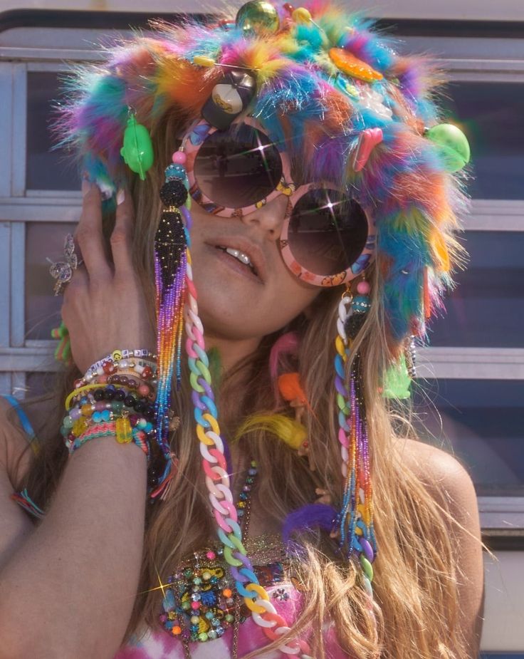 A vibrant festival outfit featuring a colorful furry hat with neon accents, paired with oversized round sunglasses and layered beaded jewelry, evoking a Grateful Dead concert vibe with Dancing Bears and hippie style aesthetics. Pink Rave Accessories, Weird Accessories, Edc Orlando, Sparkle Fashion, Rave Hats, Edm Music Festivals, Disco Jumpsuit, Outdoor Festival, Lost Lands