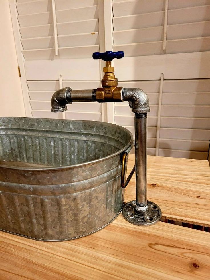 an old fashioned metal tub sitting on top of a wooden table next to a faucet