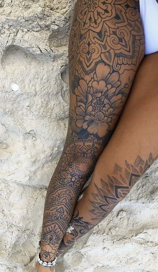 a woman's leg with tattoos on it sitting next to a rock and wearing sandals