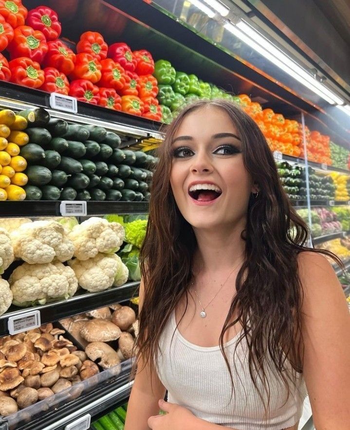 a woman standing in front of a display of fruits and vegetables at a grocery store