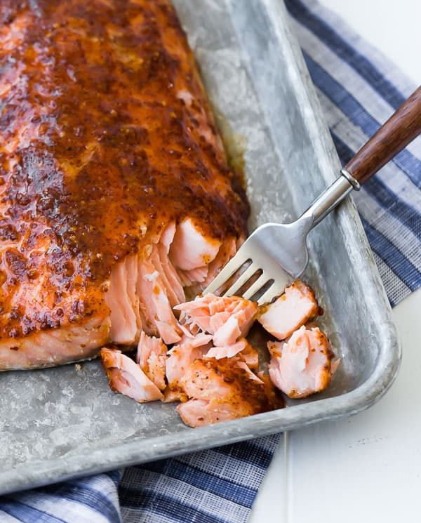 a piece of salmon with sauce on it and a fork in the pan next to it