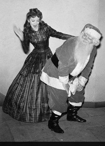 a man dressed as santa claus dancing with a woman in a long dress and hat