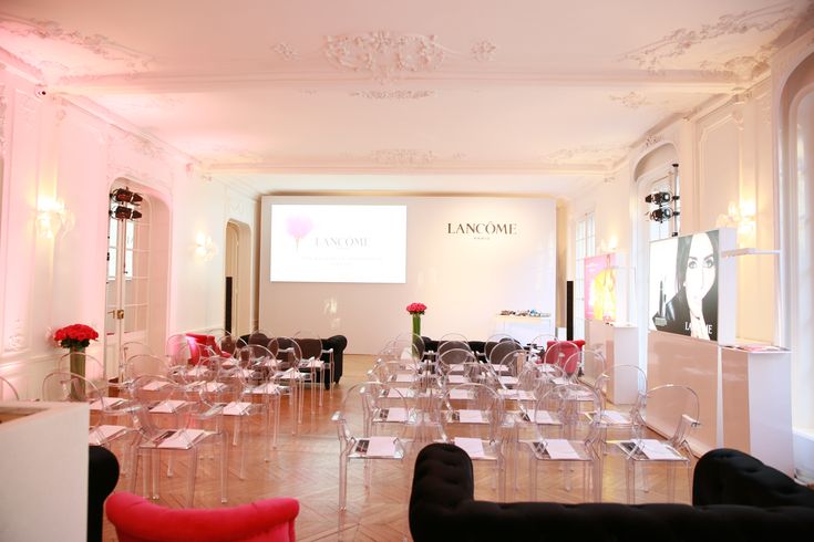 a room filled with lots of clear chairs and tables covered in pink cloths next to a projector screen