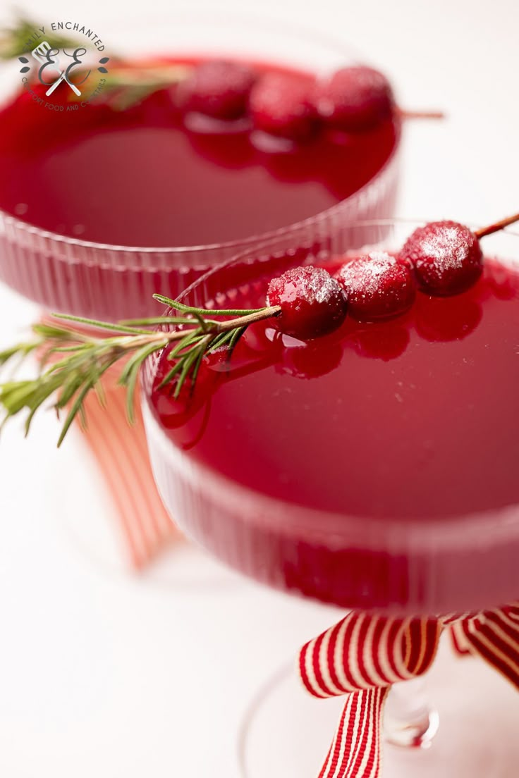 two glasses filled with red liquid and garnished with cranberry on top