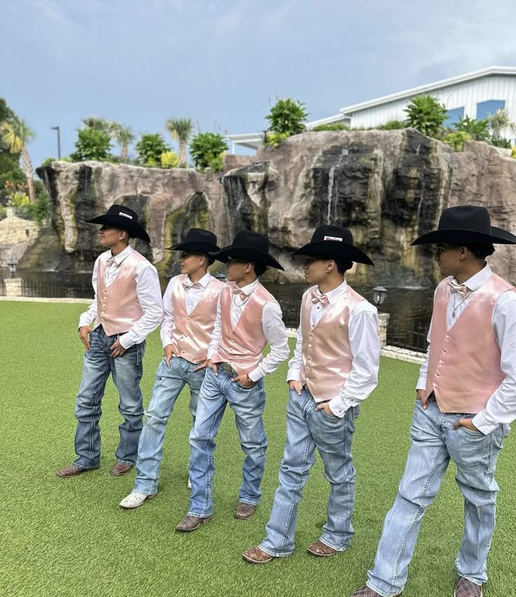 five young boys wearing pink vests and cowboy hats standing in front of a waterfall