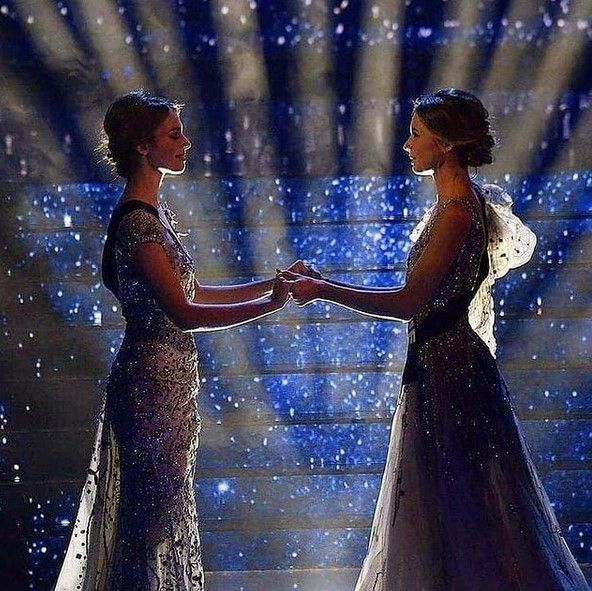 two women in evening gowns shaking hands on stage with stars and lights behind them