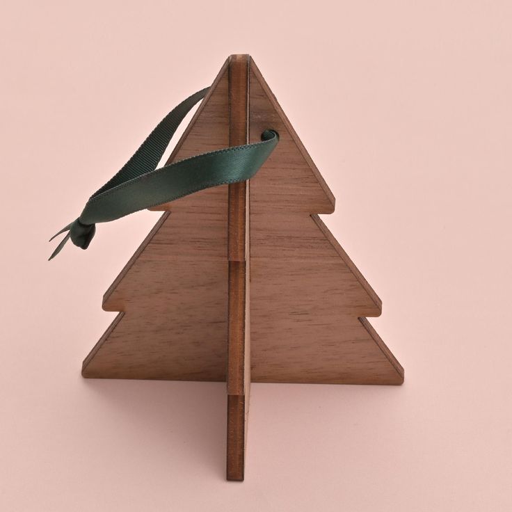 a wooden christmas tree with a green ribbon tied to it's side on a pink background