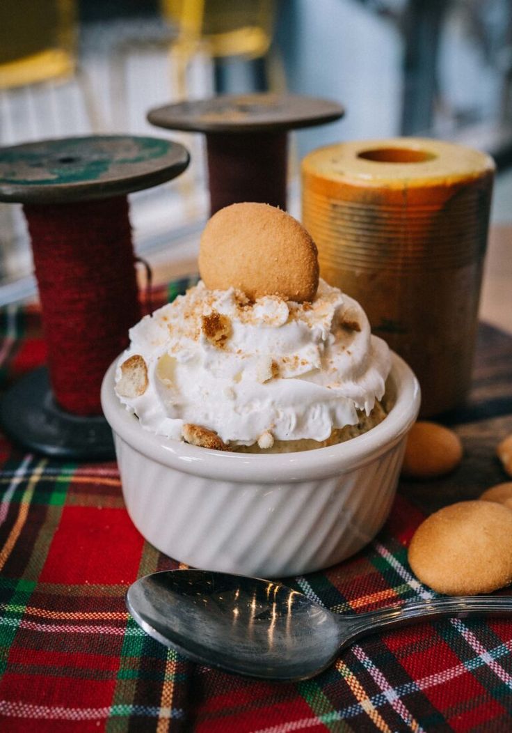 a white bowl filled with whipped cream next to two spools of thread on a table