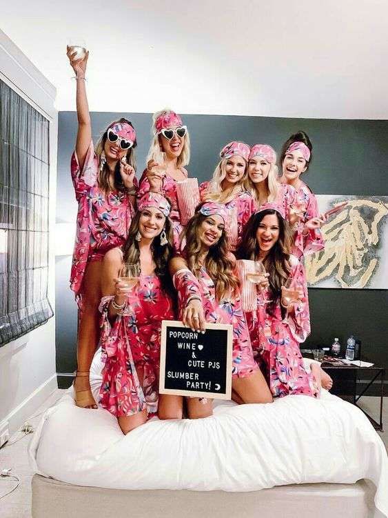 a group of women in matching pink robes posing for a photo on a white bed