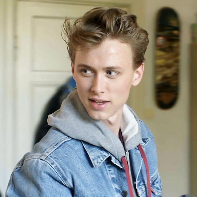 a young man wearing a denim jacket and looking at the camera