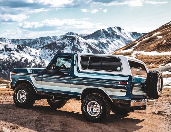 a truck parked on the side of a dirt road in front of snow covered mountains