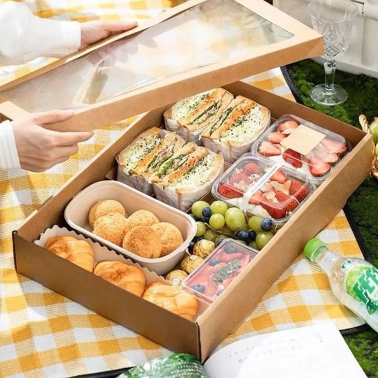 an open box filled with lots of food on top of a table next to other foods