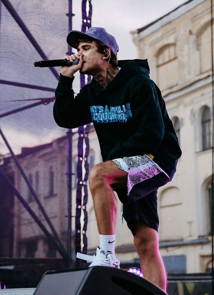 a man standing on top of a stage with a microphone in his hand and wearing a purple hat