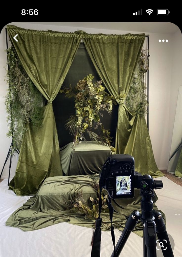 a camera set up in front of a bed with green drapes and flowers on it