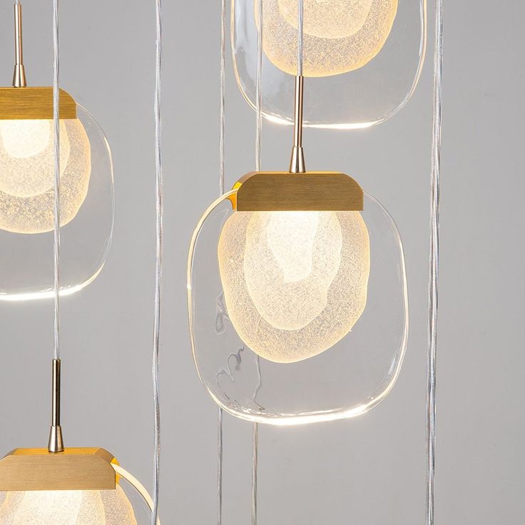 three clear glass and wood pendants hanging from strings with light bulbs in the middle