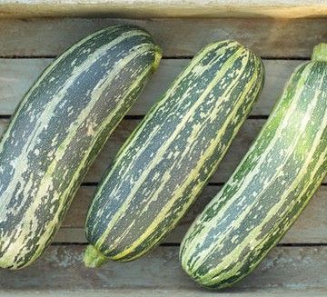 three green and yellow striped cucumbers on a wooden crate, with one zucchini in the foreground