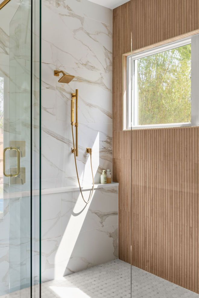 a bathroom with marble walls and flooring, shower head, and glass enclosed tub