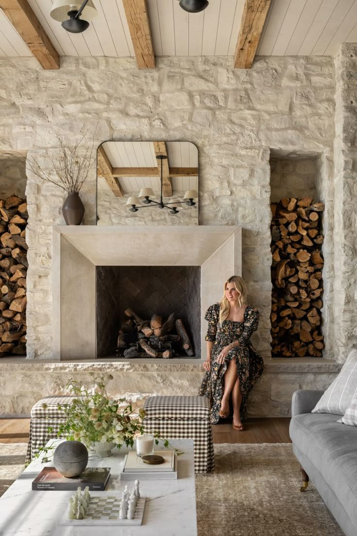 a woman sitting on a couch in front of a fire place with logs behind her