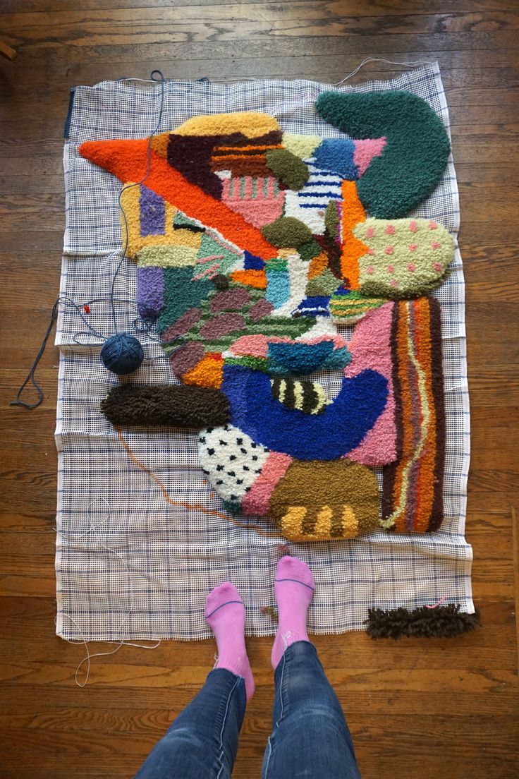 a person standing on a wooden floor next to a pile of rugs and knitting needles