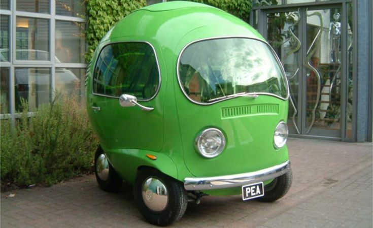 a small green van parked in front of a building with plants growing on it's side