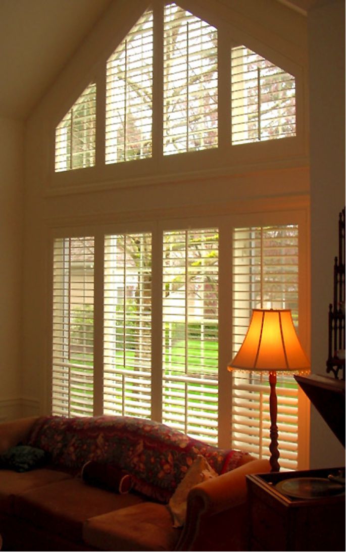 a living room filled with furniture and windows covered in wooden shutters, next to a lamp