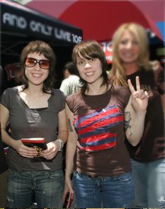 three women posing for the camera in front of a red bus with two peace signs