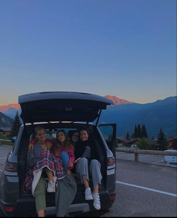 four people sitting in the back of a van with mountains in the background at sunset