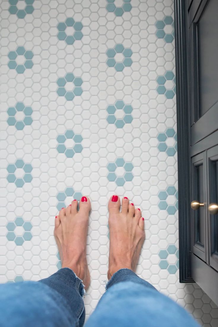 a person with red nail polish standing in front of a tiled wall and floor area