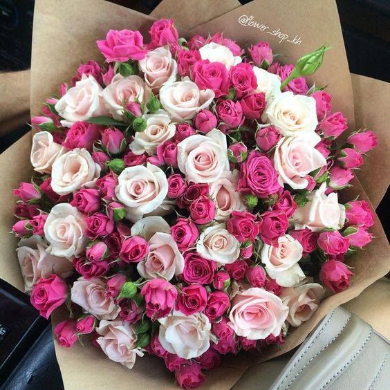 a bouquet of pink and white roses in someone's hand on the car seat