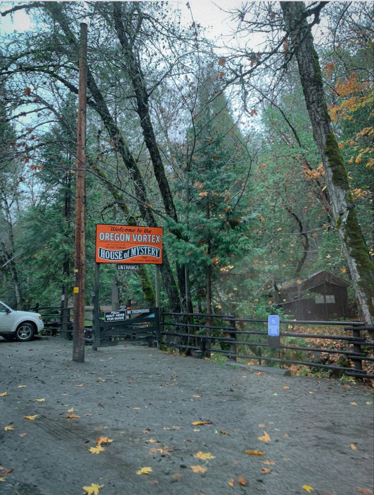 an orange and white sign is in front of a fence with cars parked behind it