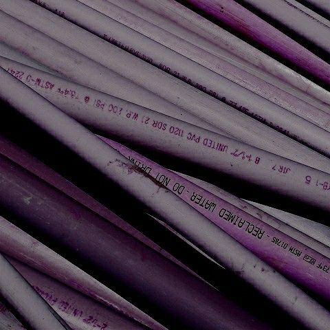 many purple pipes are stacked together in a pile and one has writing on the end