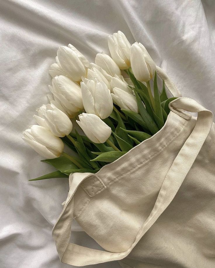 white tulips in a tote bag laying on a bed with the top half open