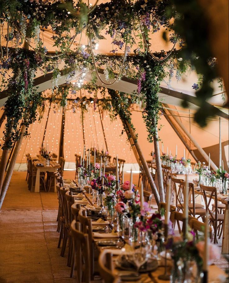 the inside of a tent with tables and chairs set up for a wedding reception, decorated with greenery