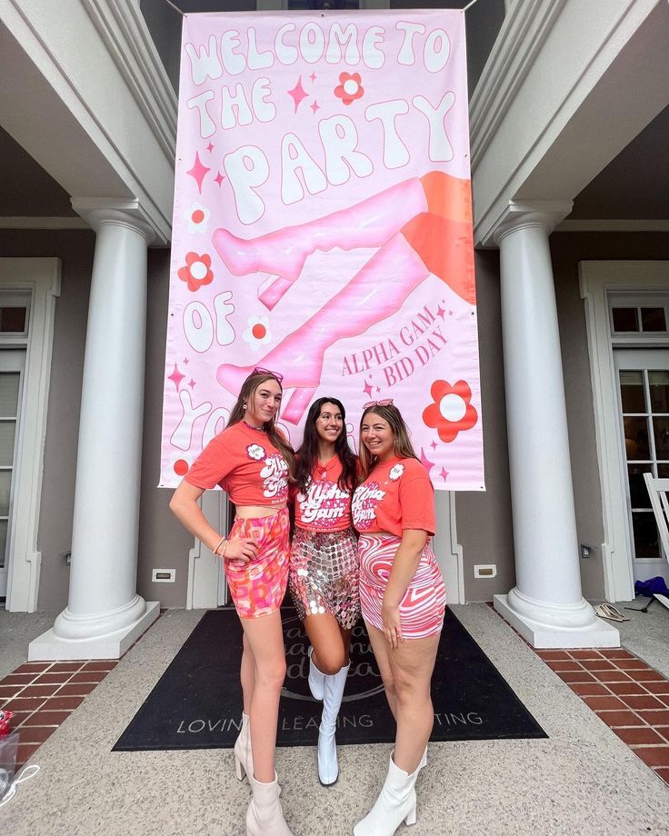 two women standing in front of a welcome to the party sign