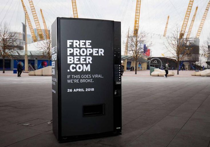 a free proper beer com vending machine sitting on the sidewalk in front of construction cranes