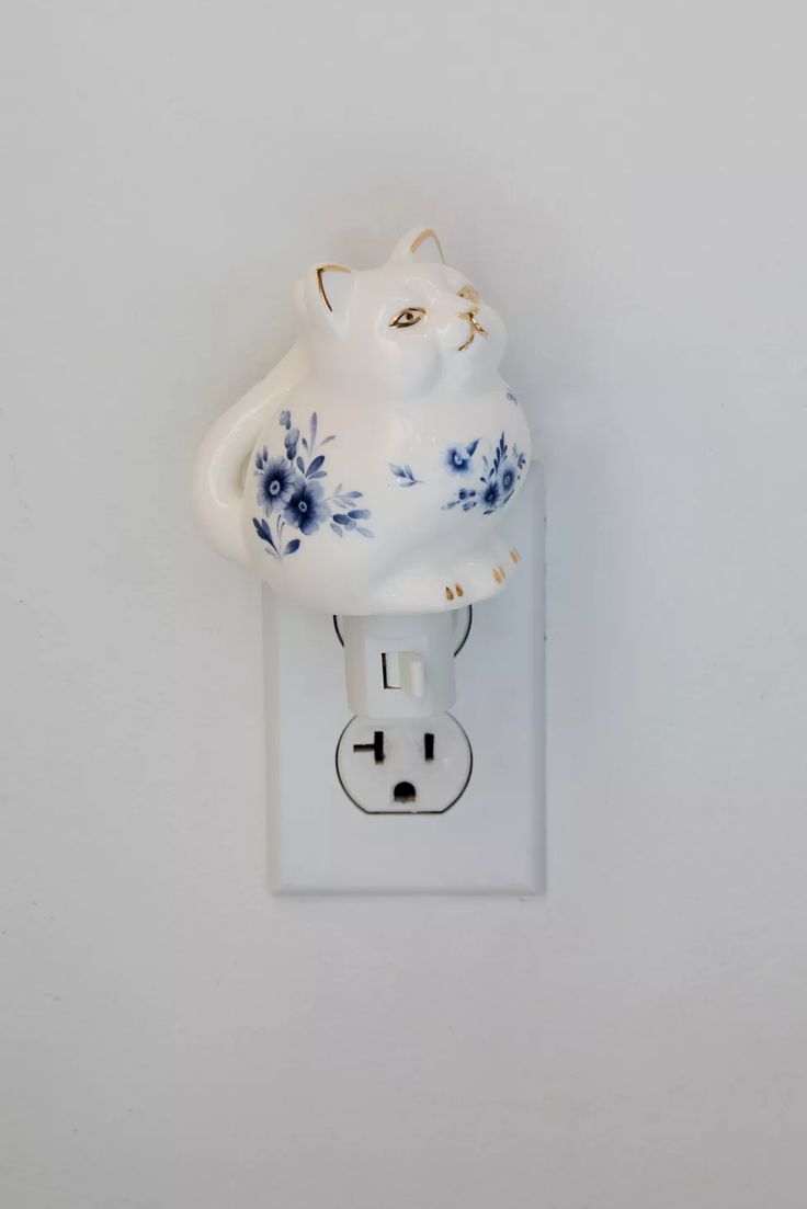 a white and blue cat plugged in to a wall outlet with flowers on it