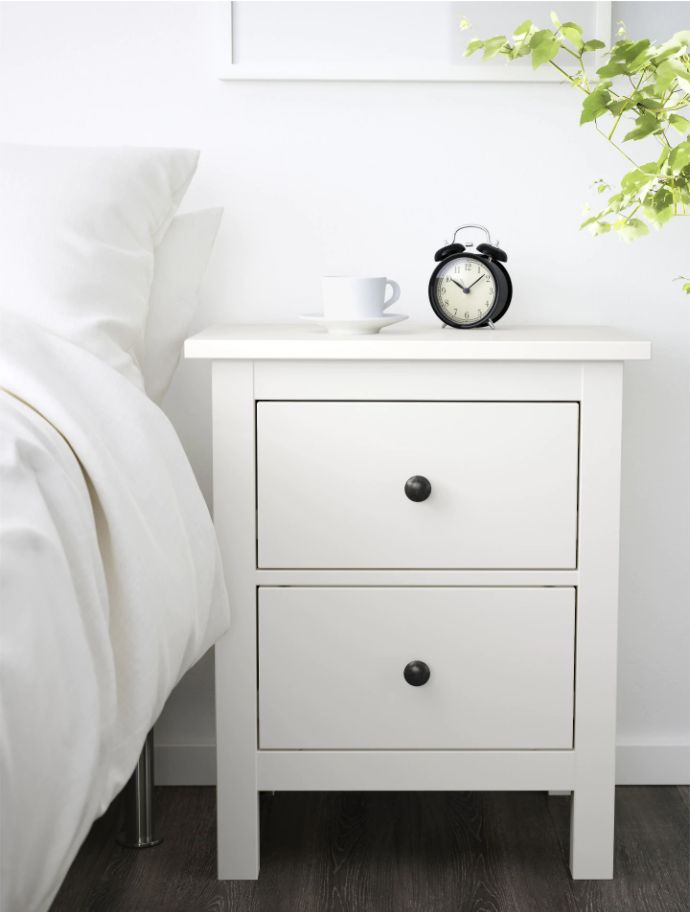 a white nightstand with a clock on it next to a bed and potted plant