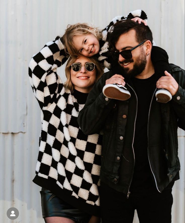 a man standing next to a woman in front of a white wall with a black and white checkered sweater