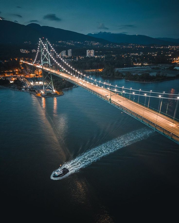 an aerial view of a bridge at night with the lights on and boats in the water below