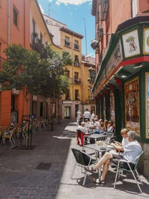 people are sitting at tables on the sidewalk in an alleyway with shops and restaurants