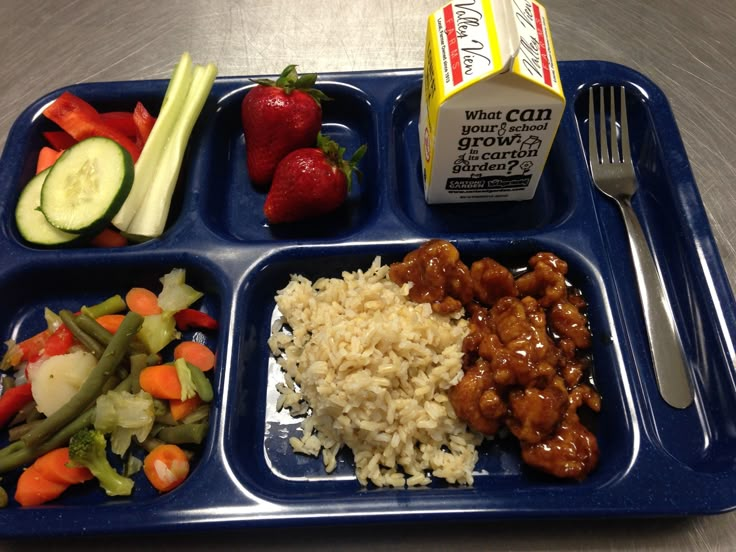 a blue plastic tray with rice, meat and veggies next to a carton of milk